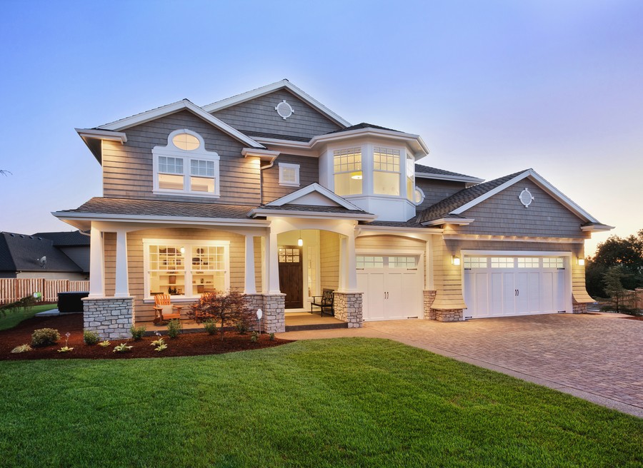 A house in the evening viewed from the front yard with all the lights on inside.