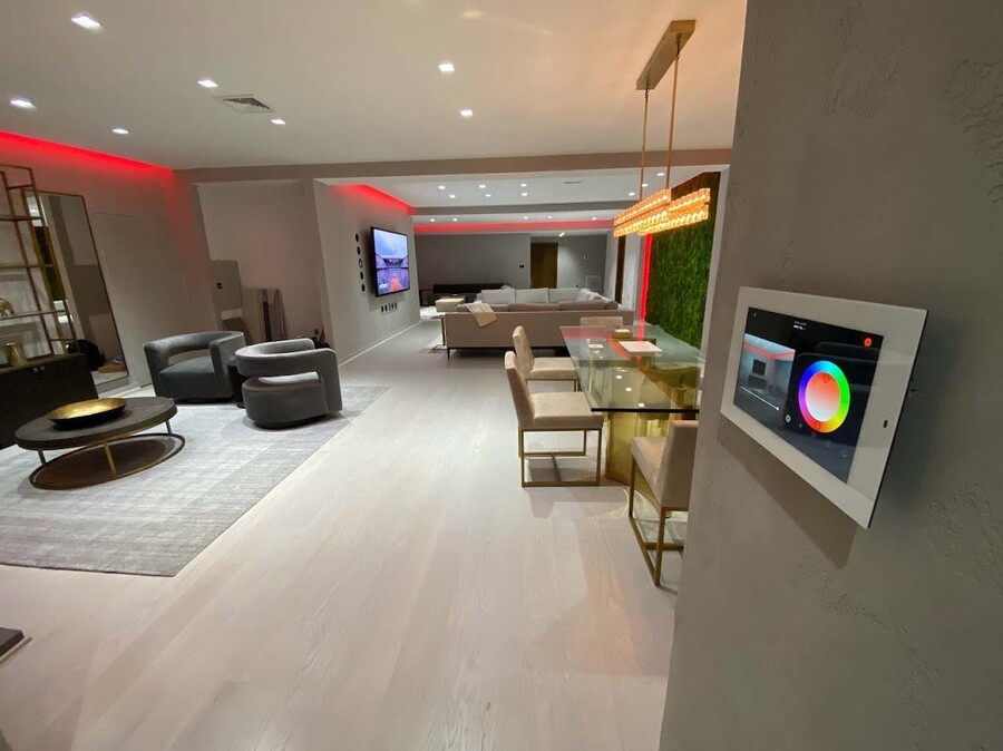 Modern living room with recessed lighting, color-changing LED accents, and a wall-mounted smart lighting control panel.