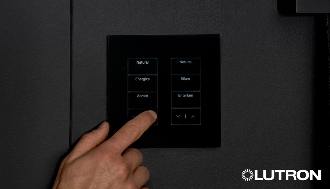 Hand pressing a Lutron Palladiom keypad with preset lighting scene options on a black wall panel.
