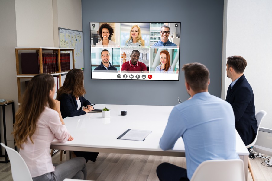 Team in a small meeting room video conferencing with remote employees.  