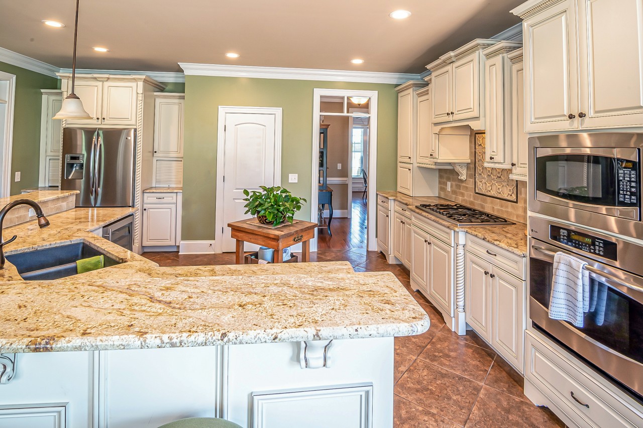 A beautiful kitchen with granite countertops, white wooden cabinets, and gorgeous recessed lighting fixtures.