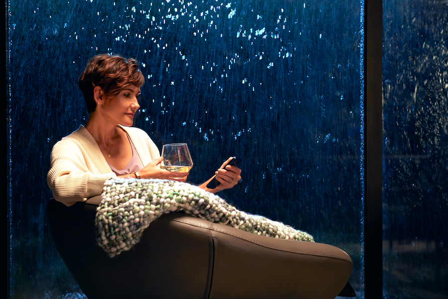 A woman relaxing in a chair with a glass of wine looking at her phone during a rainstorm.